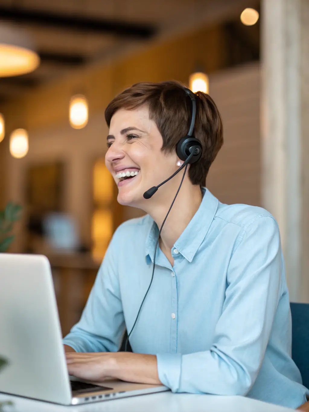 A professional headshot of a smiling customer service agent wearing a headset, working in a modern contact center environment. The agent is assisting a caller, and the image conveys efficiency and helpfulness.